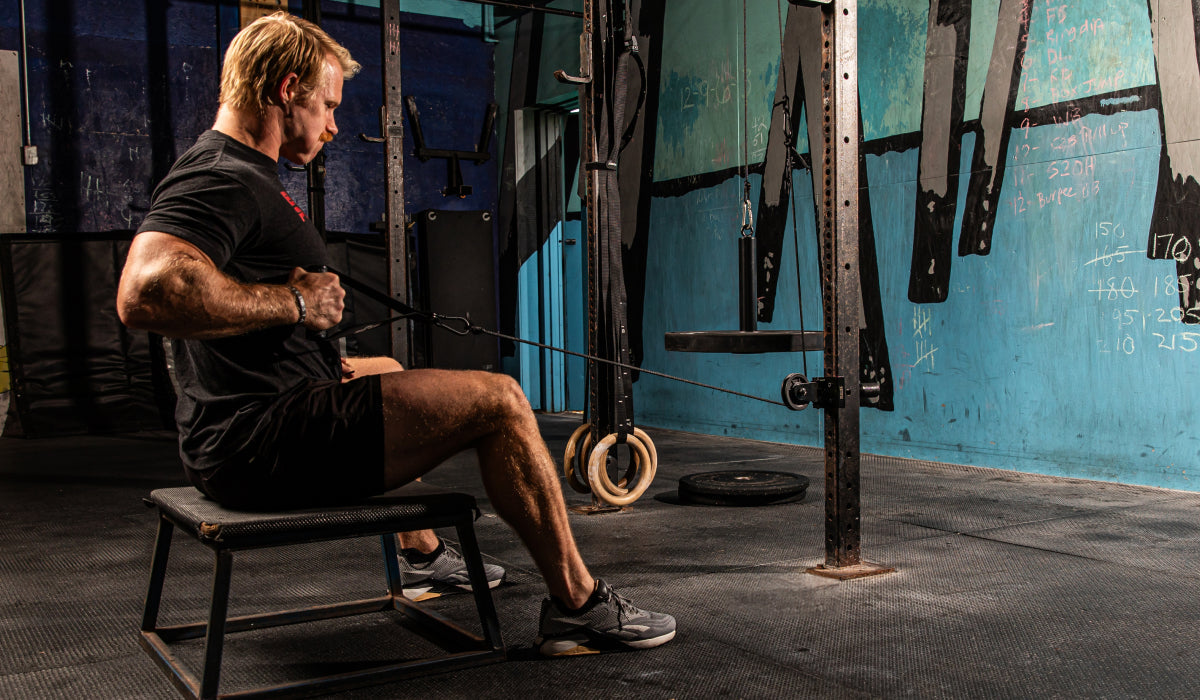 Man performing a seated row exercise using a pulley machine in a home gym. The background features a blue wall with workout notes and a tire.