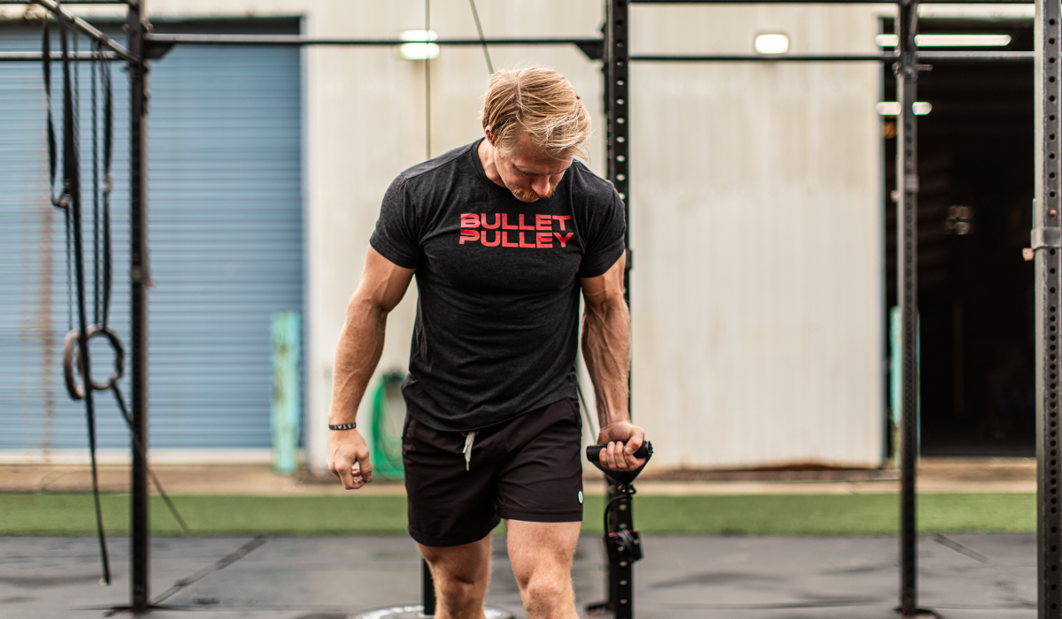 Athletic man wearing a Bullet Pulley shirt performing a cable machine exercise in a gym, highlighting strength training, muscle development, and functional fitness.