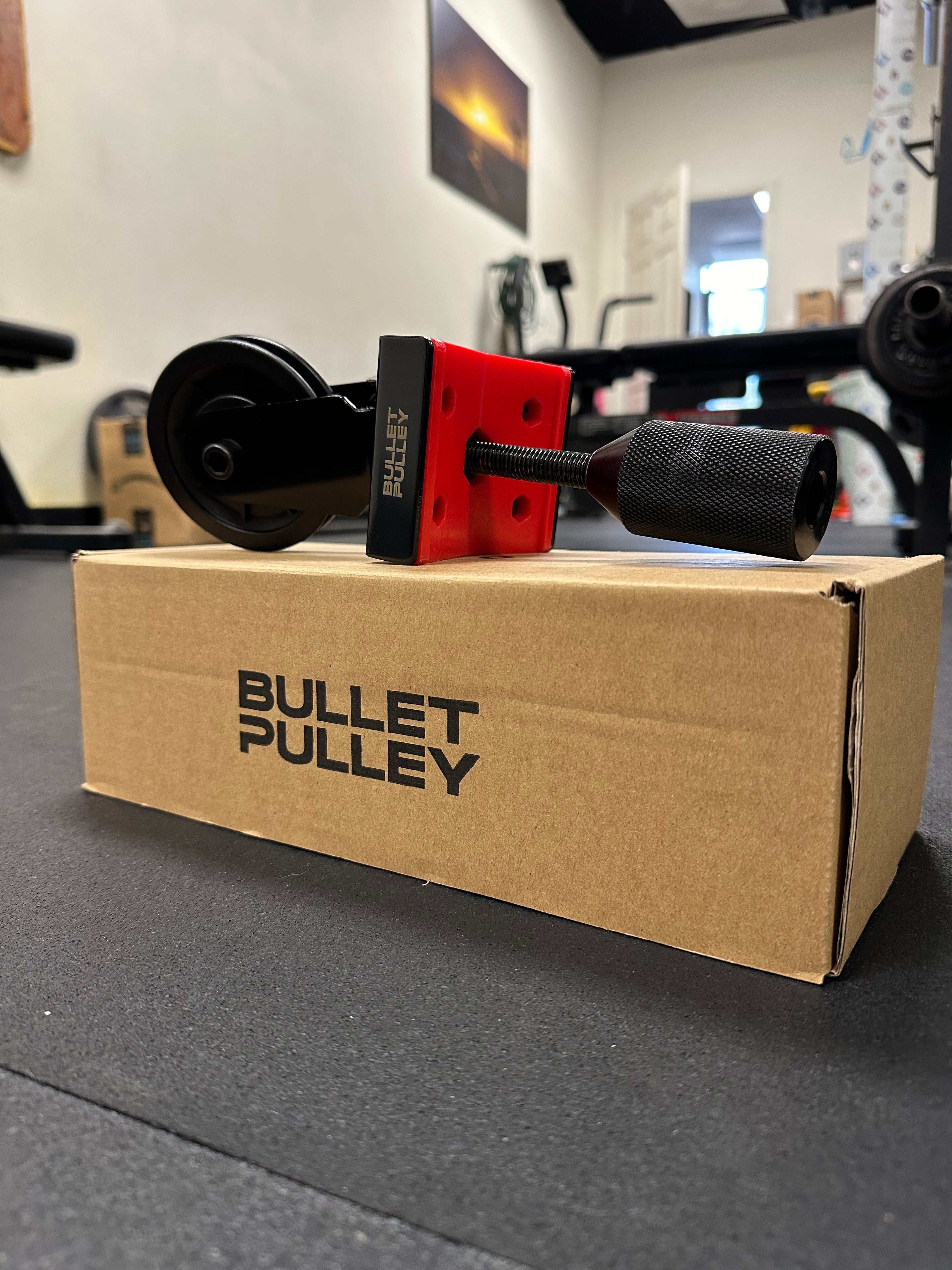 Bullet Pulley home gym equipment with sturdy design, showcased in a home gym setting. The pulley system is displayed on a cardboard box, emphasizing durability and strength for home workouts.