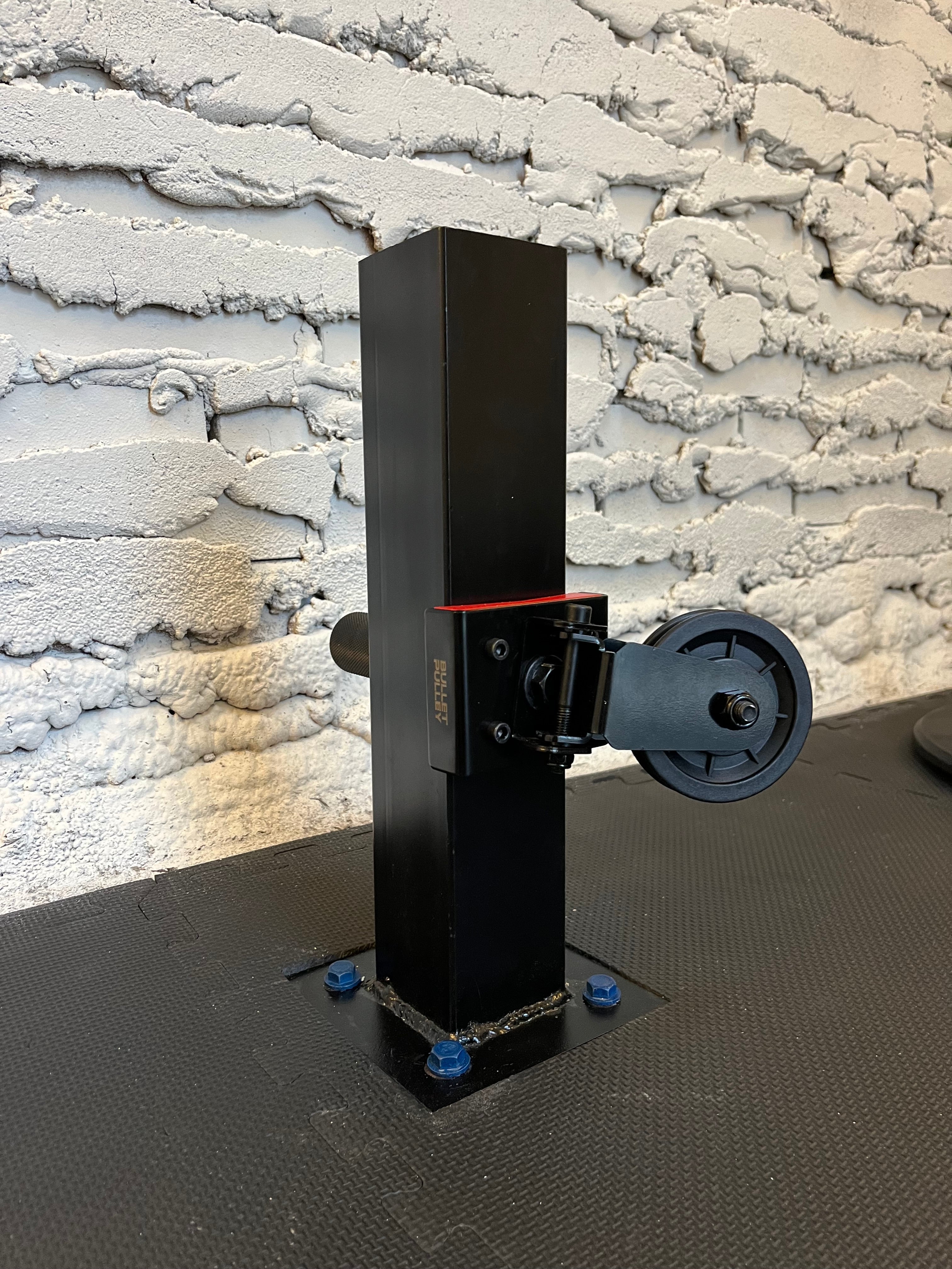 Home gym pulley system mounted on a black post with adjustable settings. Sturdy construction and compact design for home fitness setups.