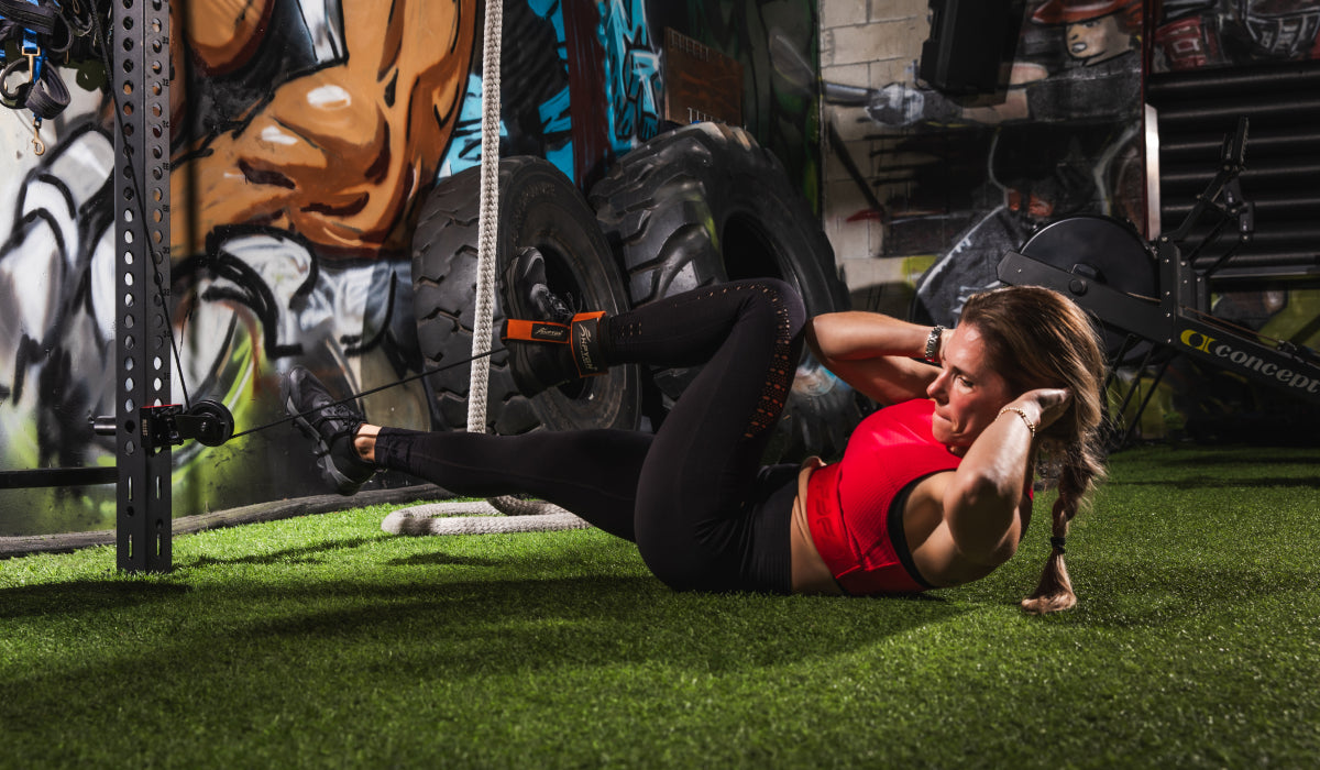 Woman performing a core workout using resistance bands in a home gym setup. The vibrant graffiti wall and tires create a dynamic background for her fitness routine.