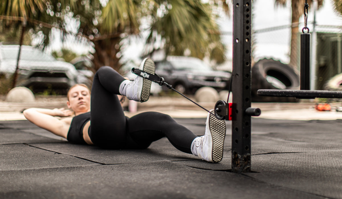 A person performing a home gym workout using a pulley system. The individual is on the floor, engaging in a low-impact exercise to target core muscles.