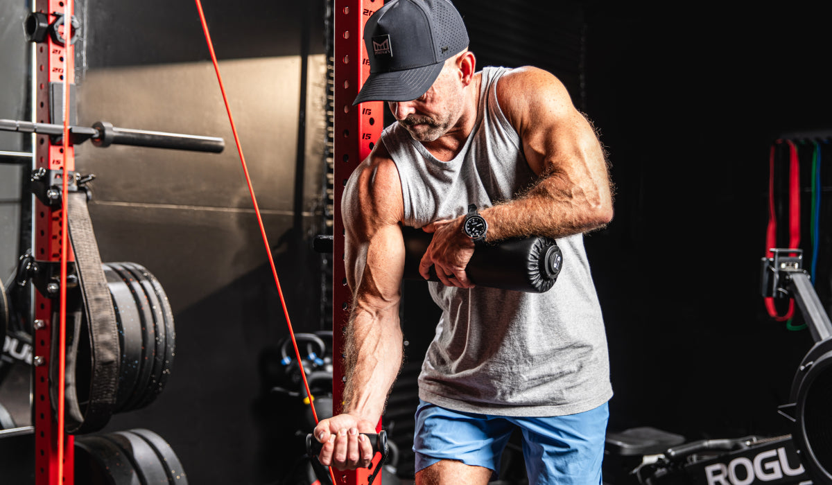 Man performing a bicep curl using a pulley system in his home gym. Fitness equipment and accessories are visible in the background.