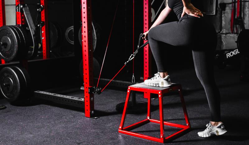"Person doing resistance band leg workout using red plyo box in gym