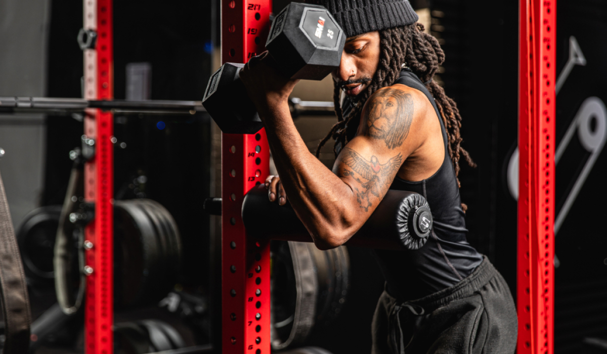 Man lifting a dumbbell in a home gym setting with red equipment. Focus on bicep strength training with weights and gym accessories.