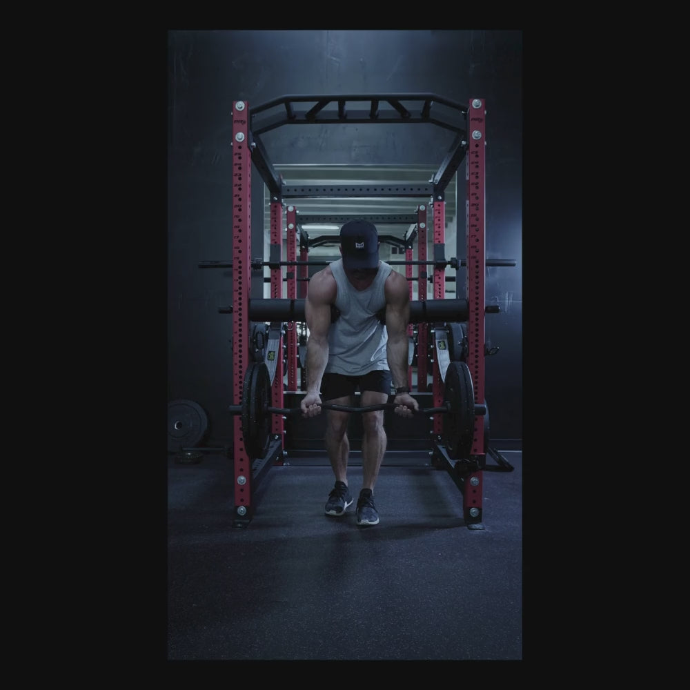Male using Bullet Pulley Anchor Pad to perform a strength training exercise with a cable system in a garage gym environment. The image highlights a muscular figure lifting weights, showcasing the versatility of the Bullet Pulley product in workout routines.