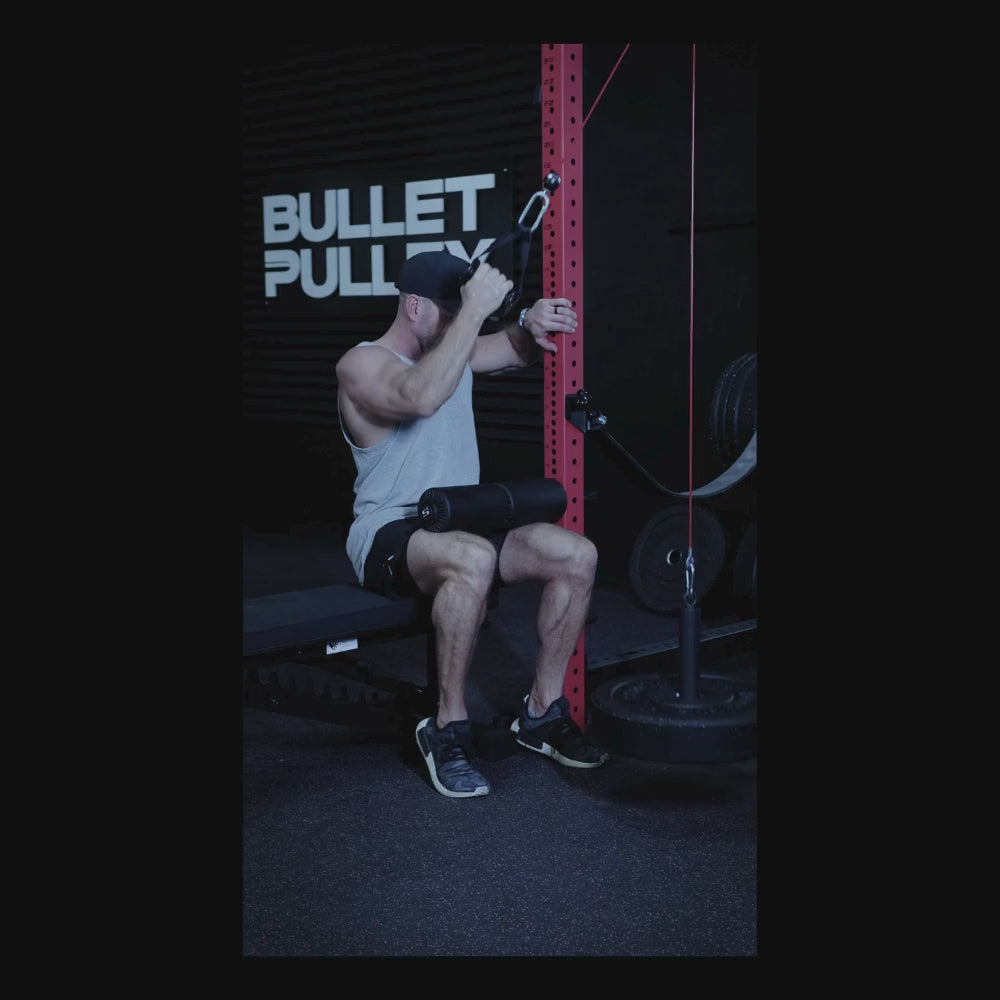 A person performing a cable exercise with the Bullet Pulley Anchor Pad, showcasing the product in use in a home gym setting with weights and equipment in the background.