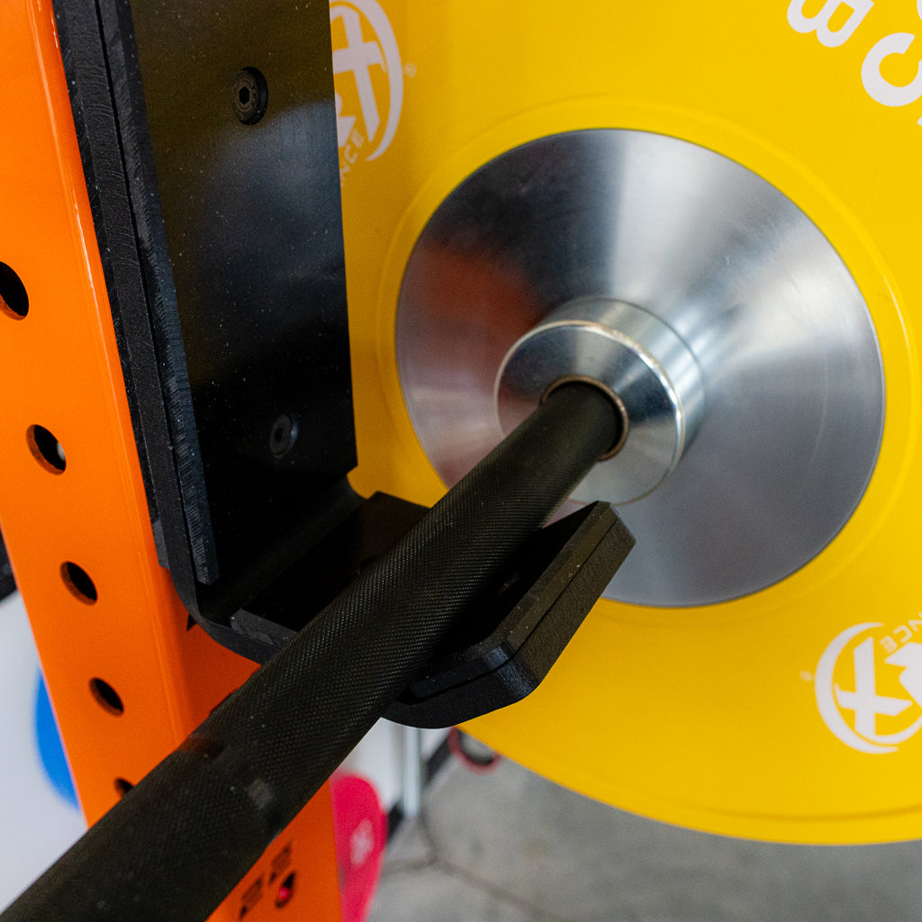 Close-up of a squat rack with a pull-up bar attachment, featuring a yellow weight plate, a black barbell, and a metal collar securely holding the bar in place, with a vibrant orange rack frame in the background.