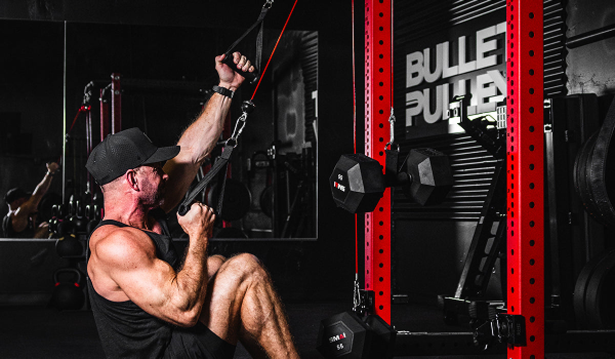 Man performing a seated cable lat pulldown using a red home gym pulley system attached to a squat rack, focusing on upper body strength in a dark gym setting.