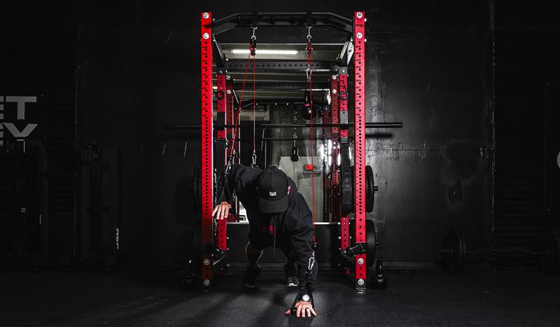 High pulley system on a red power rack used for cable-resisted crawl training in a home