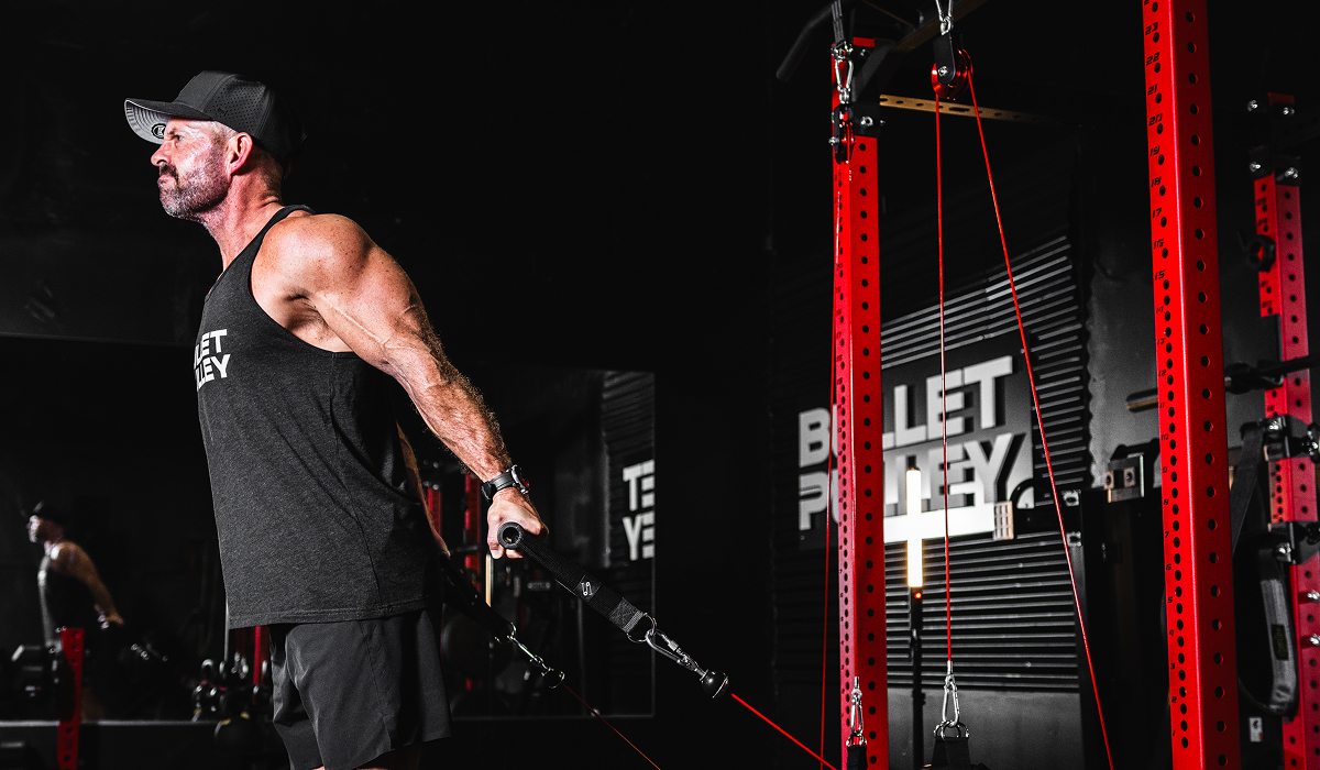 Man training with Bullet Pulley cable system in a gym, pulling handles with resistance bands to strengthen grip and upper body muscles.